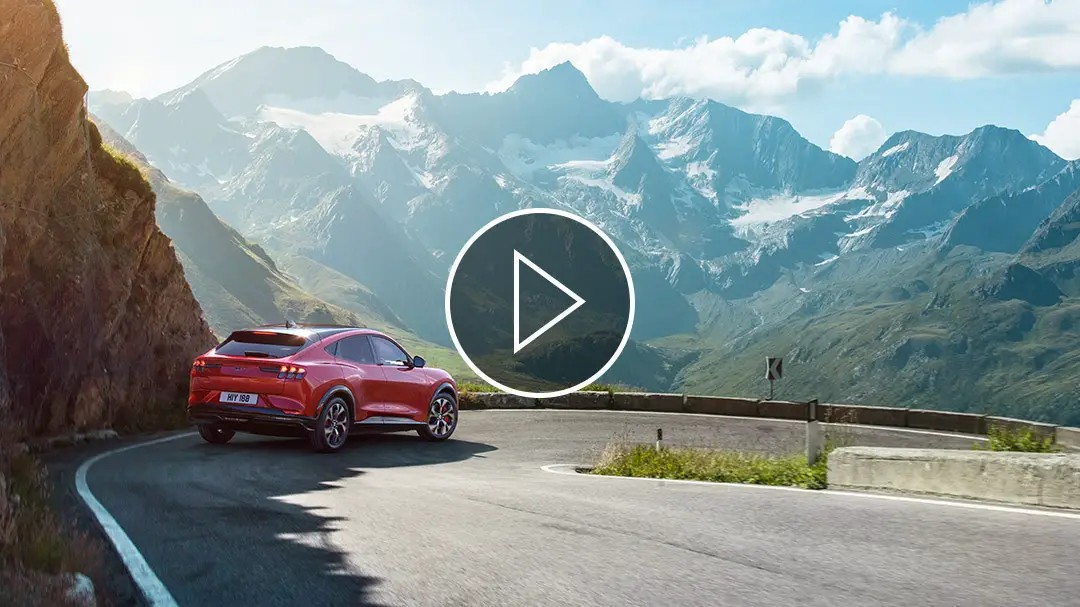 Rückansicht des Ford Mustang Mach-E, der durch eine wunderschöne Berglandschaft fährt.